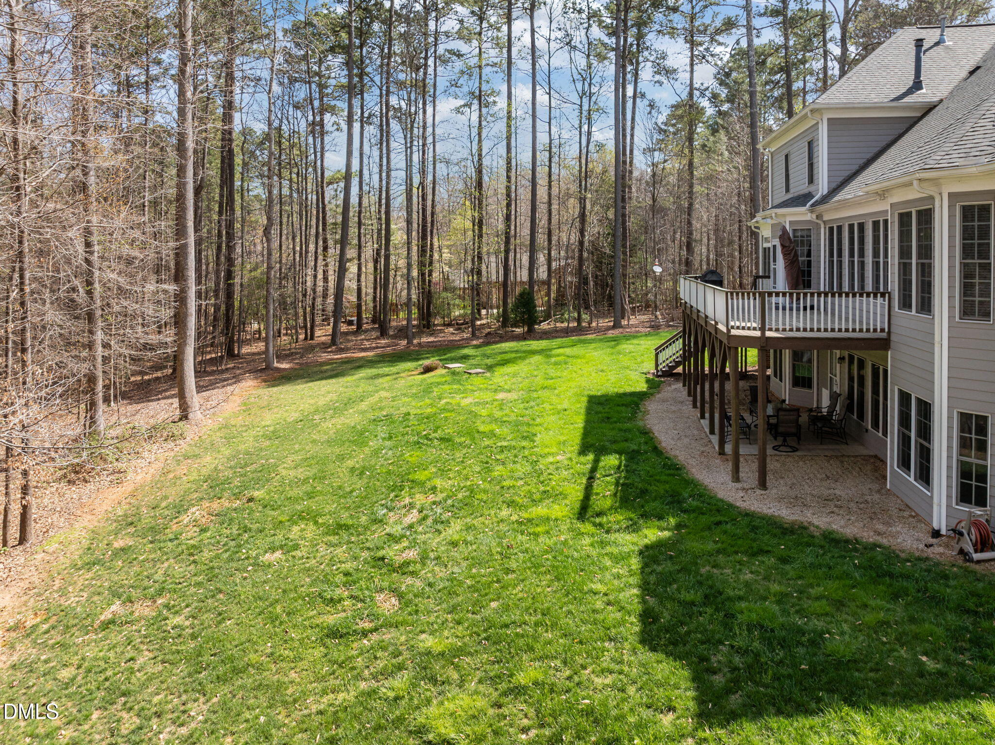 House backyard with a raised deck overlooking a broad lawn and wooded lot.