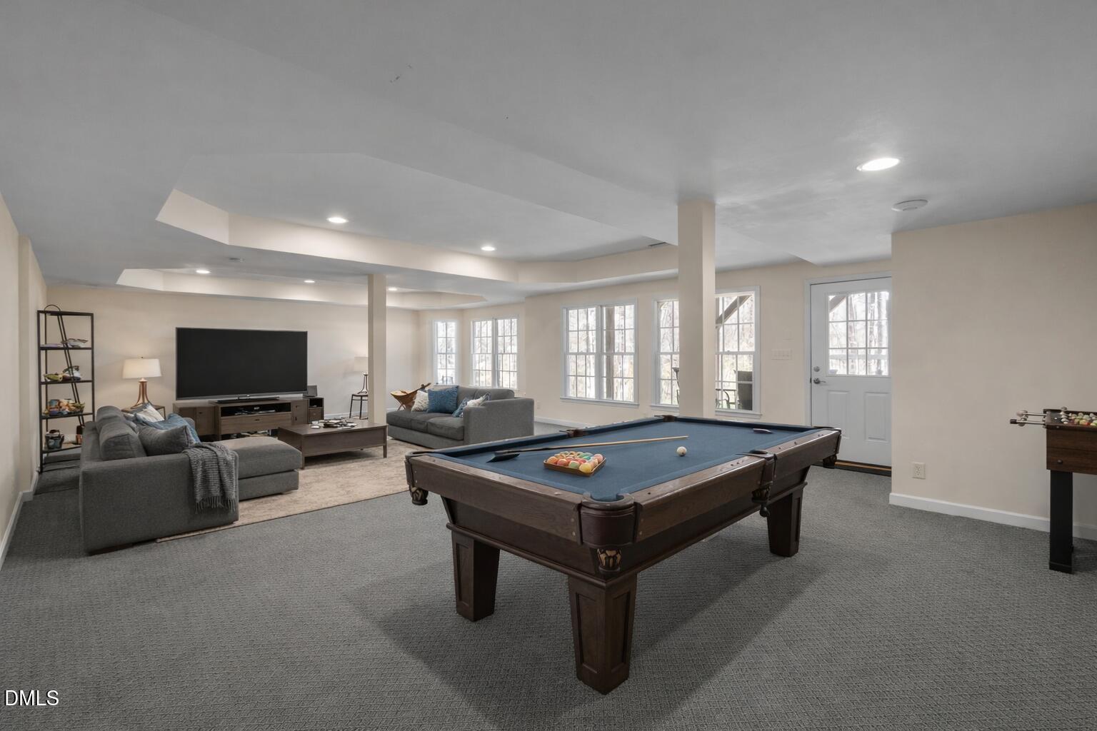 Furnished basement game room with a pool table, gray seating, television, and foosball table.