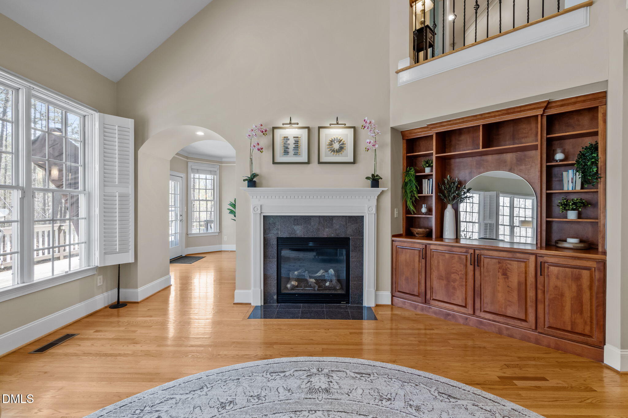 Living room with a white fireplace, built-in cherrywood shelving, tall windows, and hardwood floors.