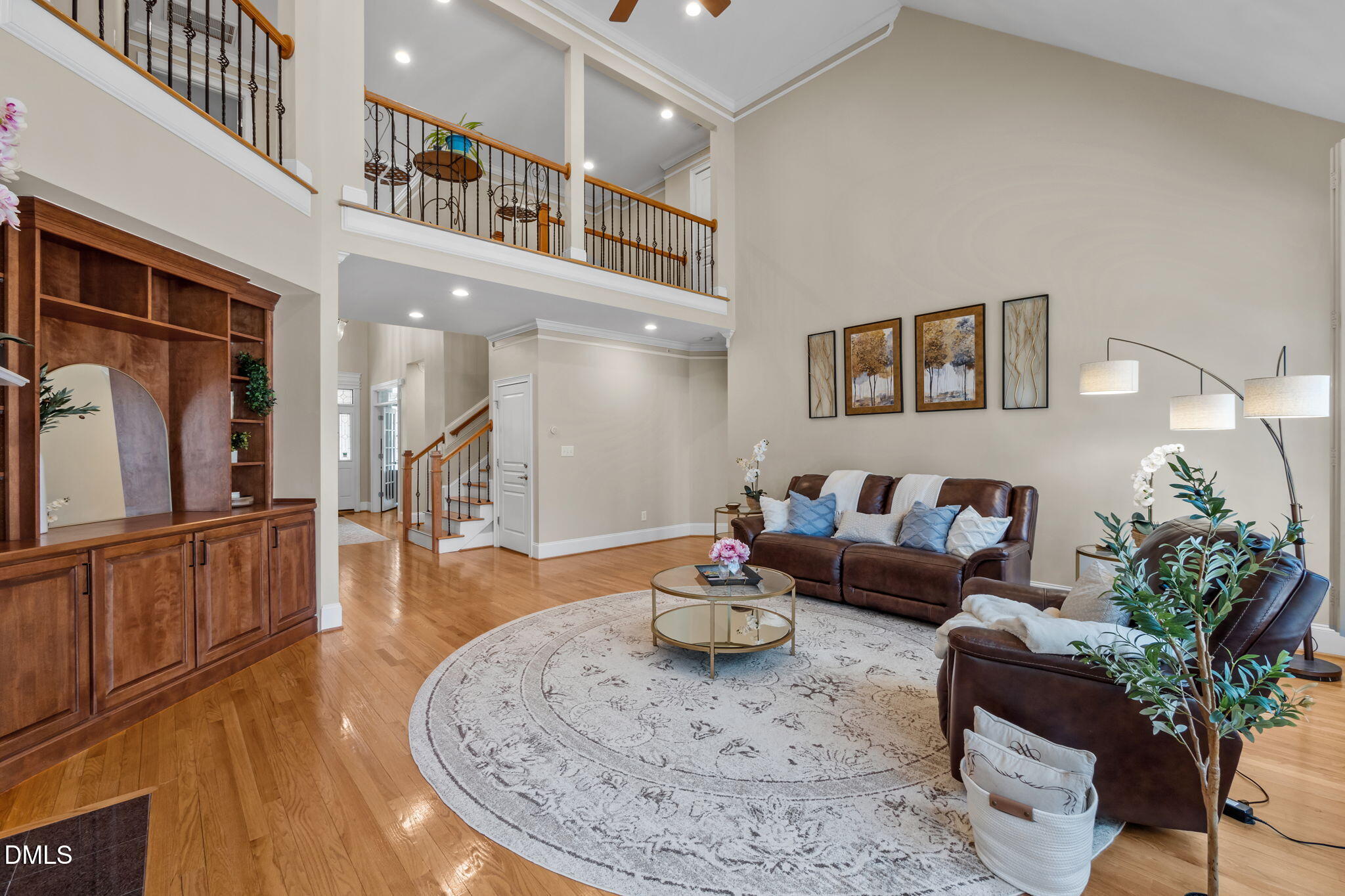 Two-story living room with a balcony, built-in wooden cabinetry, leather sofas, and hardwood floors.