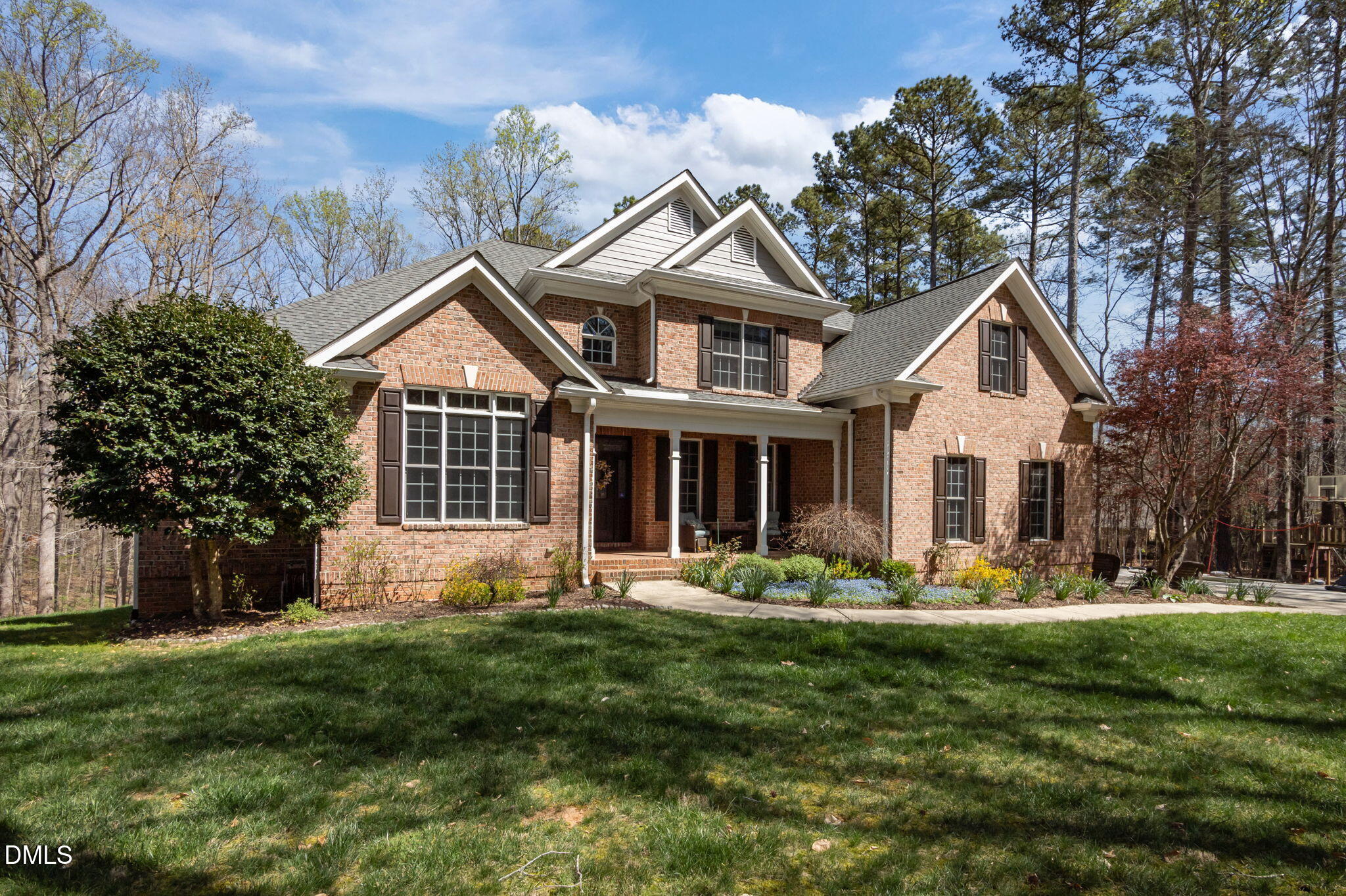 Two-story brick home with a covered porch, landscaped garden beds, and mature trees.