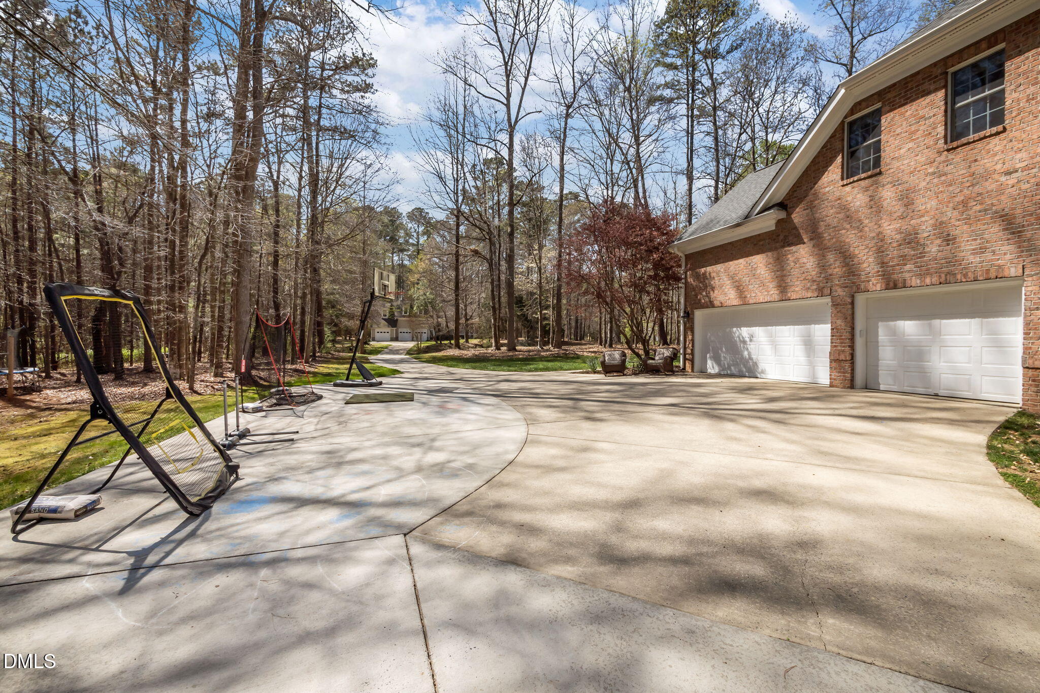 Brick home with two-car garage, broad driveway, basketball hoop, and portable sports nets.