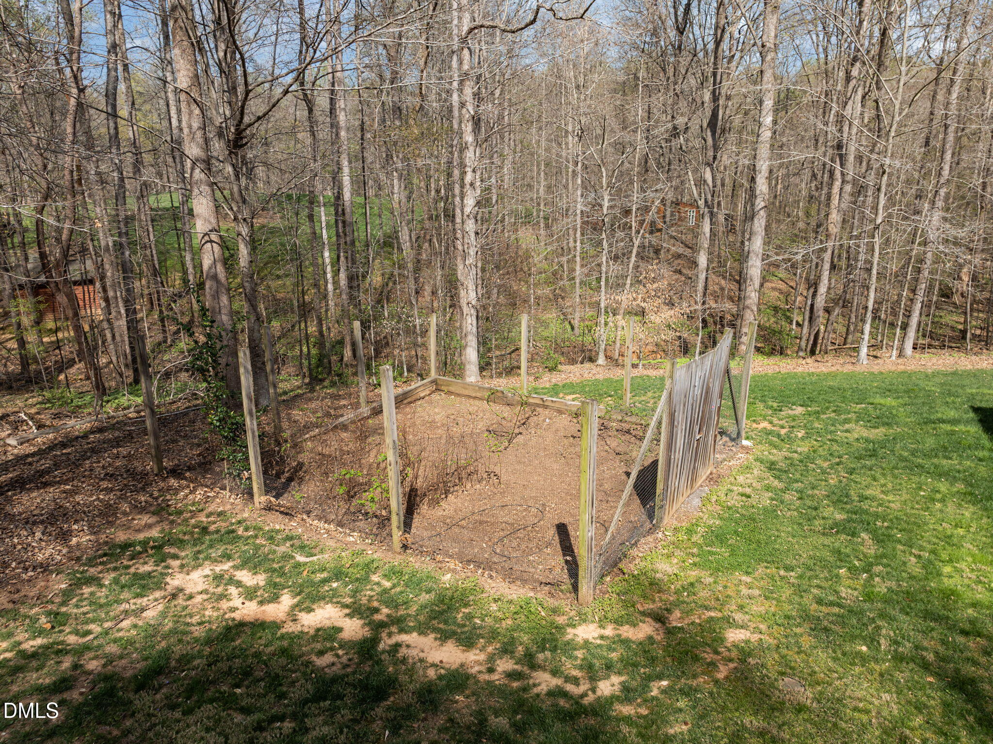 Backyard garden bed enclosed by fencing beside a lawn and leafless woods.