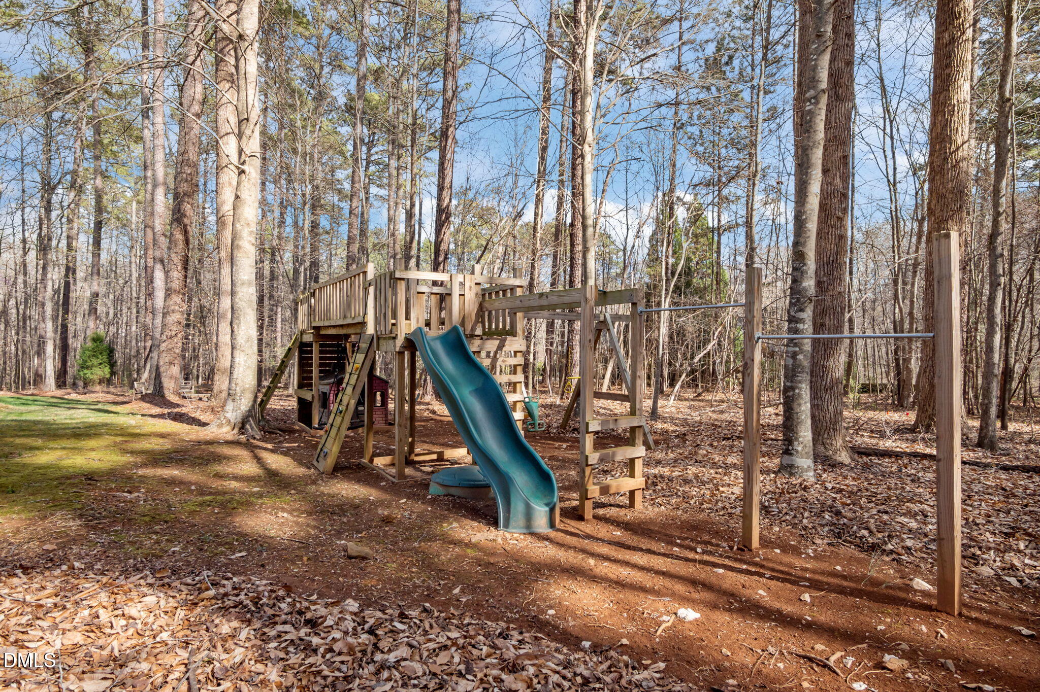 Backyard playset with a blue slide and monkey bars in a wooded yard.