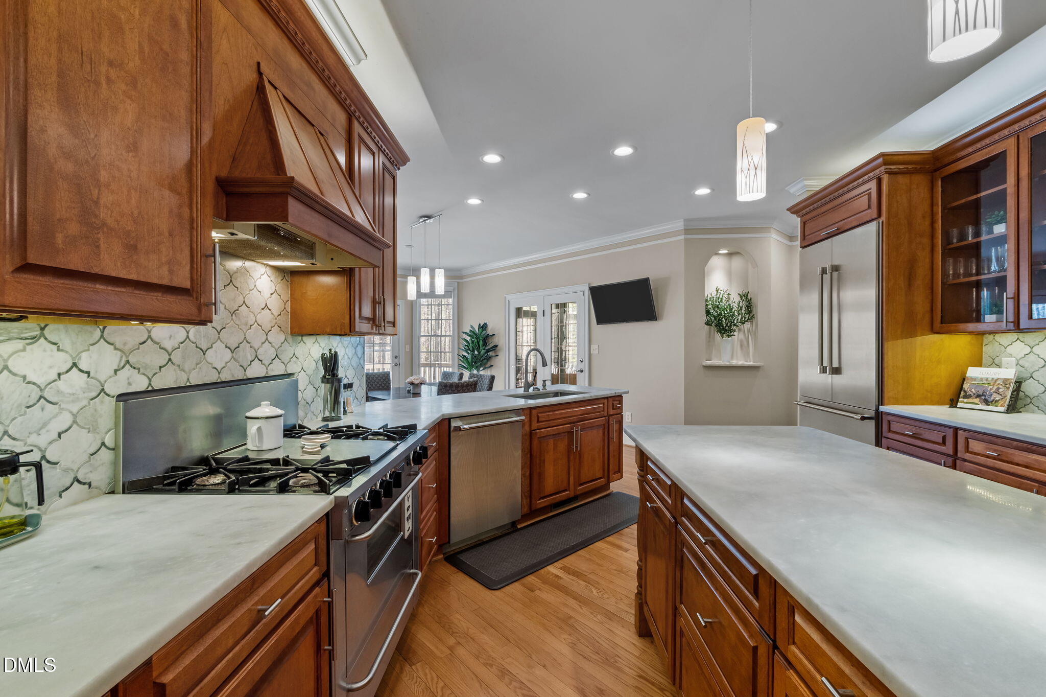 Kitchen with rich wood cabinetry, pale stone counters, a large island, and stainless steel appliances.