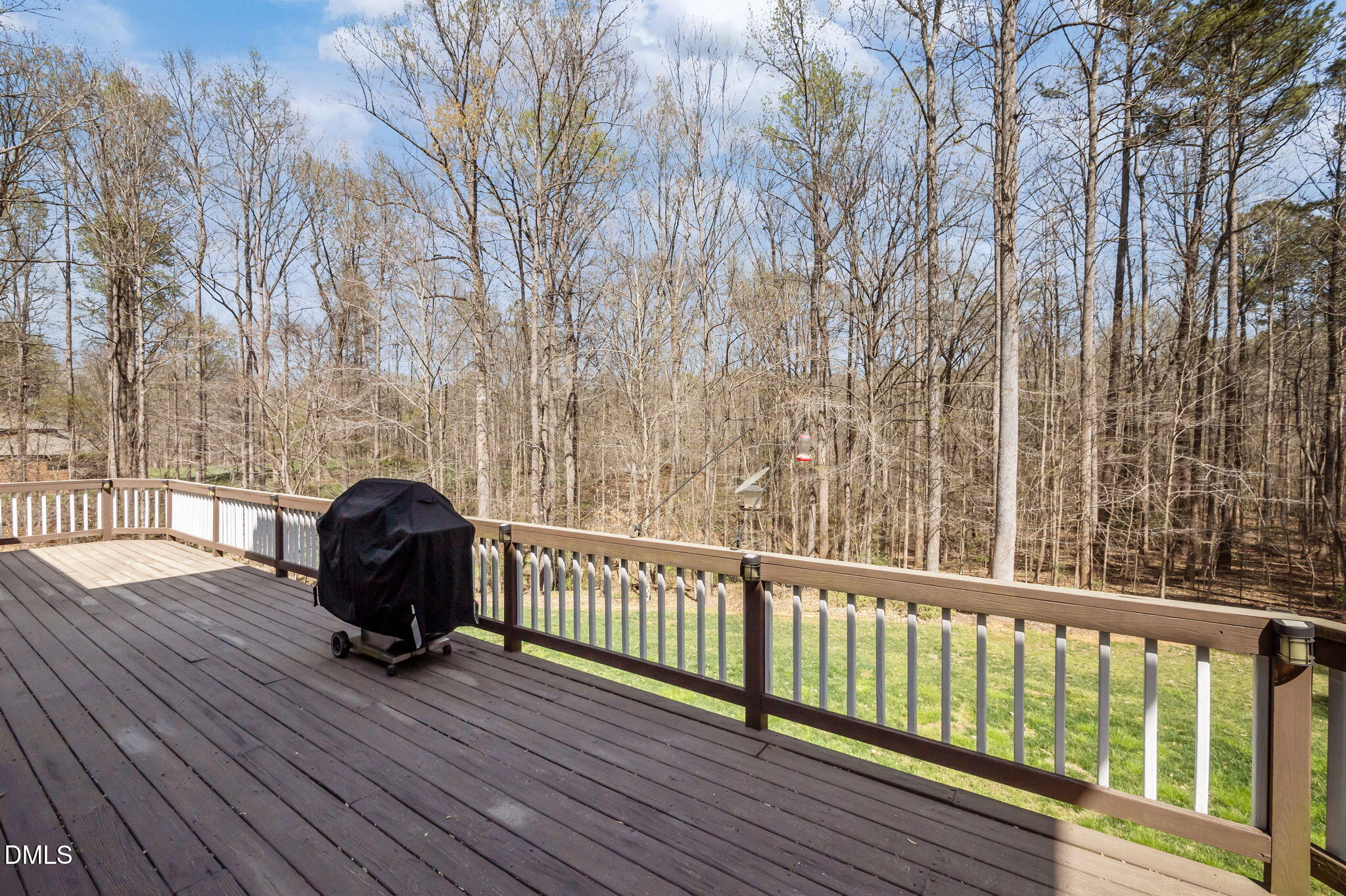 Wood deck overlooking a leafless wooded backyard, with a covered grill and bird feeder.