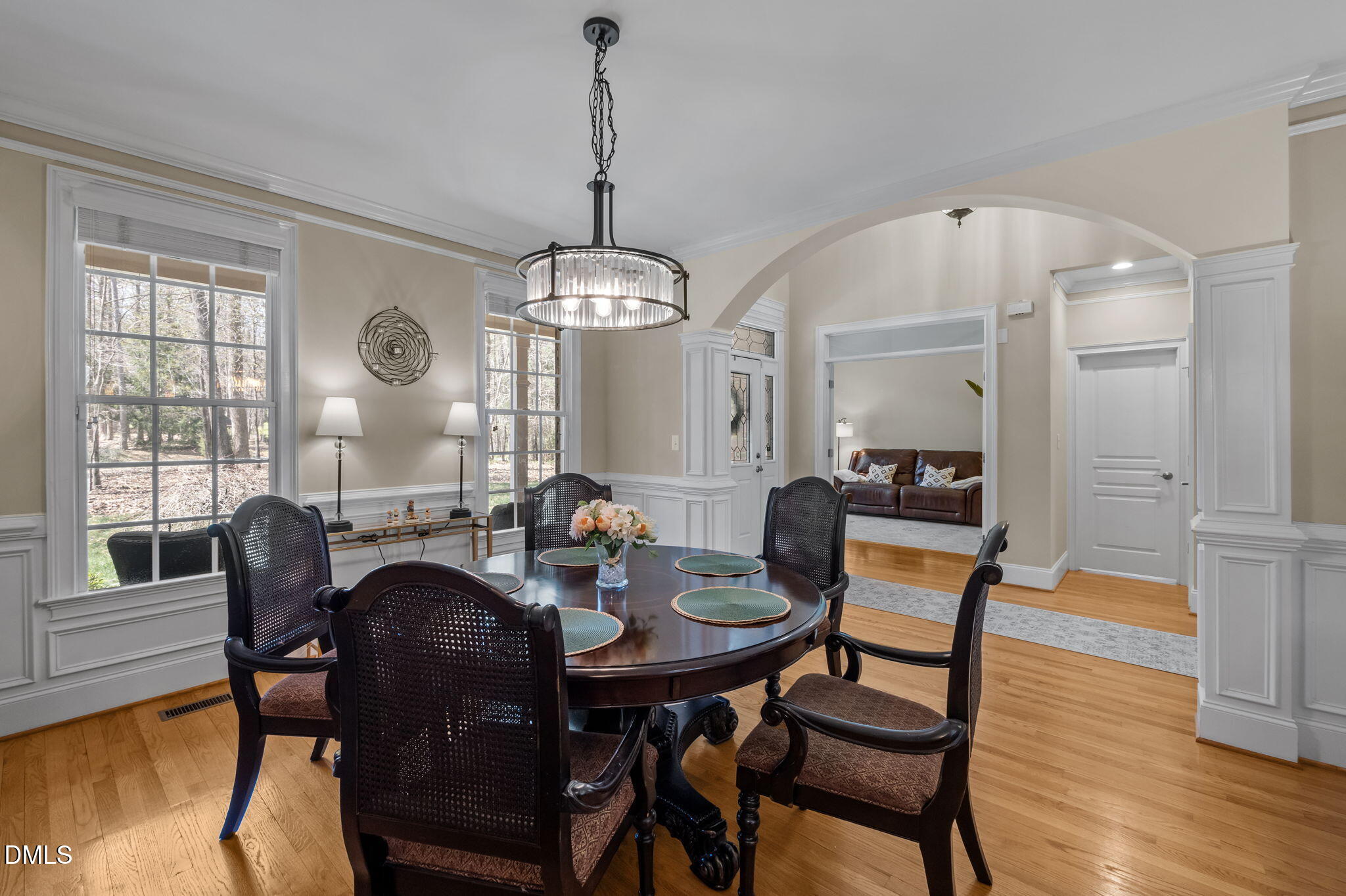 Dining room with an oval table, crystal chandelier, tall windows, and an arched opening to the living room.