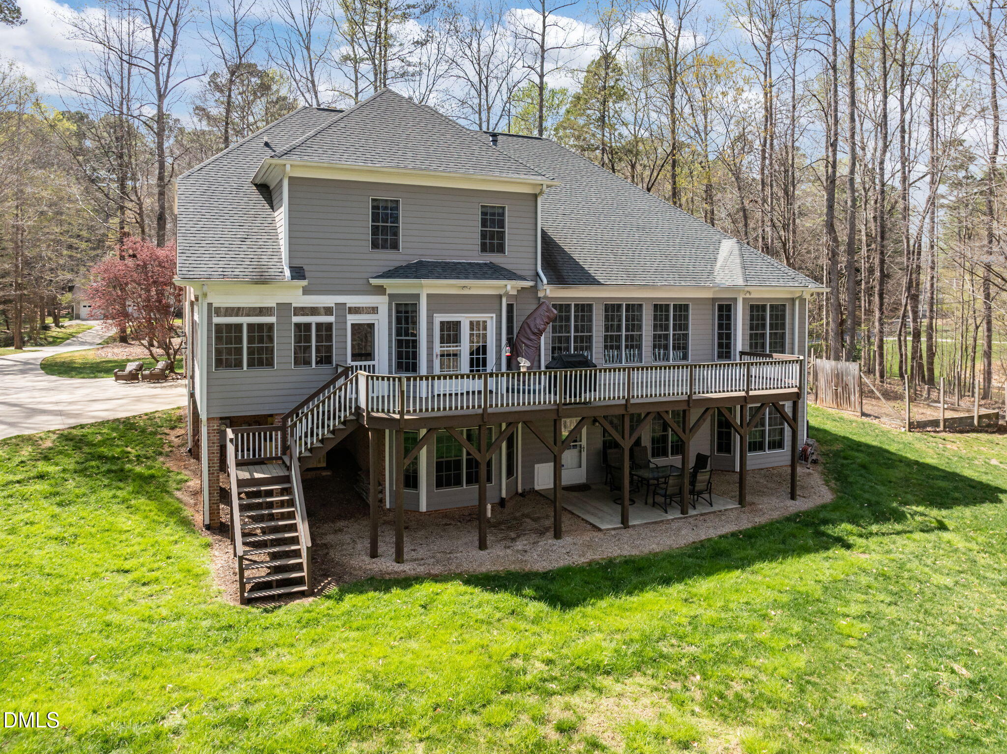 Rear of a gray two-story home with a raised deck and stairs, surrounded by trees.