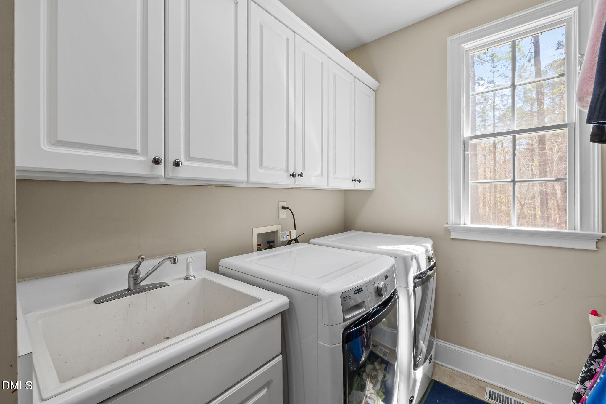 Laundry room with a utility sink, white cabinets, and washer and dryer beside a large window.