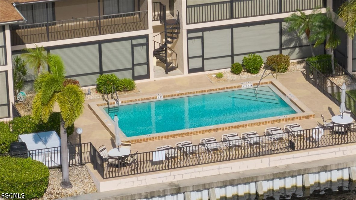 Outdoor condominium pool with a tiled deck, seating, palm trees, and a canal nearby.