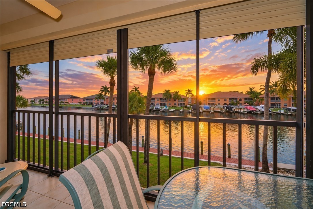 Screened lanai overlooking a canal at sunset, with palm trees and waterfront homes beyond.