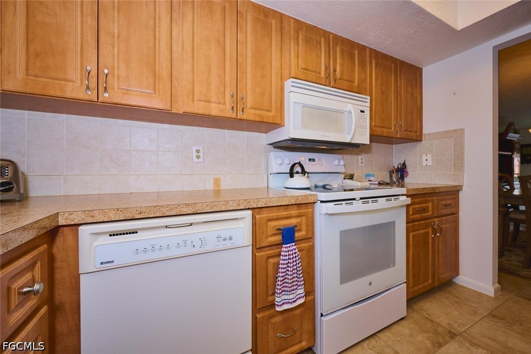 Kitchen with honey-colored wood cabinets, white appliances, and a light tile backsplash.