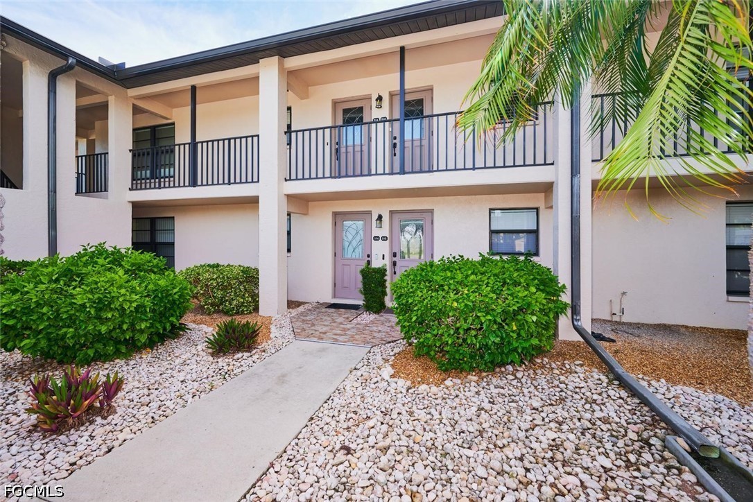 Two-story condominium entrance with covered balconies, pink doors, and a stone-landscaped walkway.