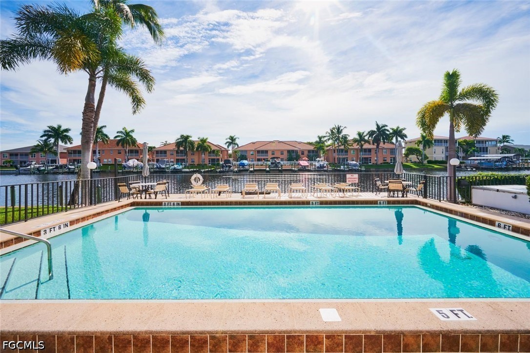 Outdoor pool beside a canal, with palm trees and condominium buildings across the water.