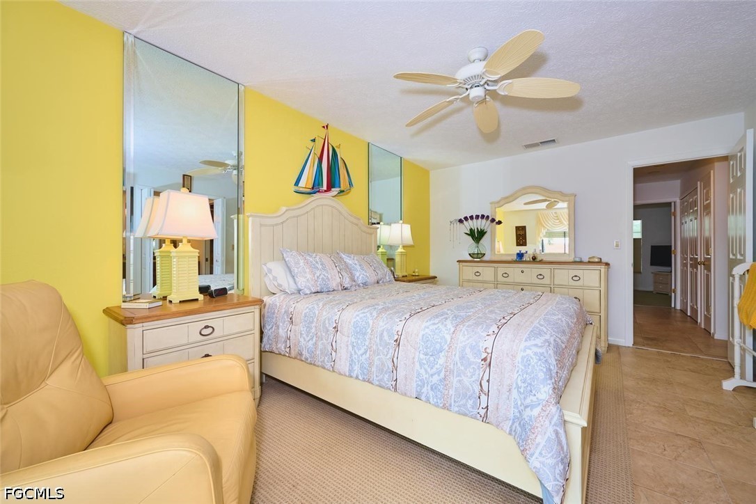 Furnished bedroom with mirrored panels, a yellow accent wall, and a large bed with patterned bedding.