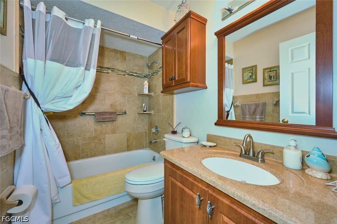 Bathroom with tiled tub and shower, white curtain, and wood vanity beneath a large mirror.