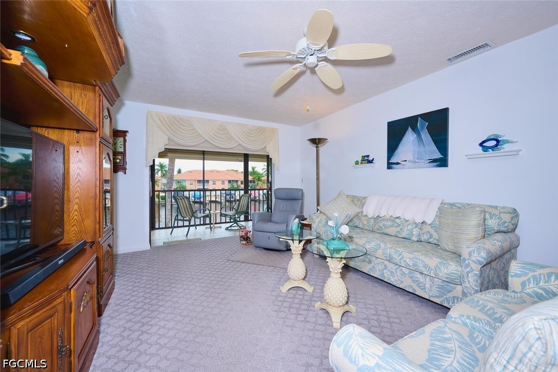 Living room with patterned sofas and a wooden entertainment center, opening onto a furnished balcony.