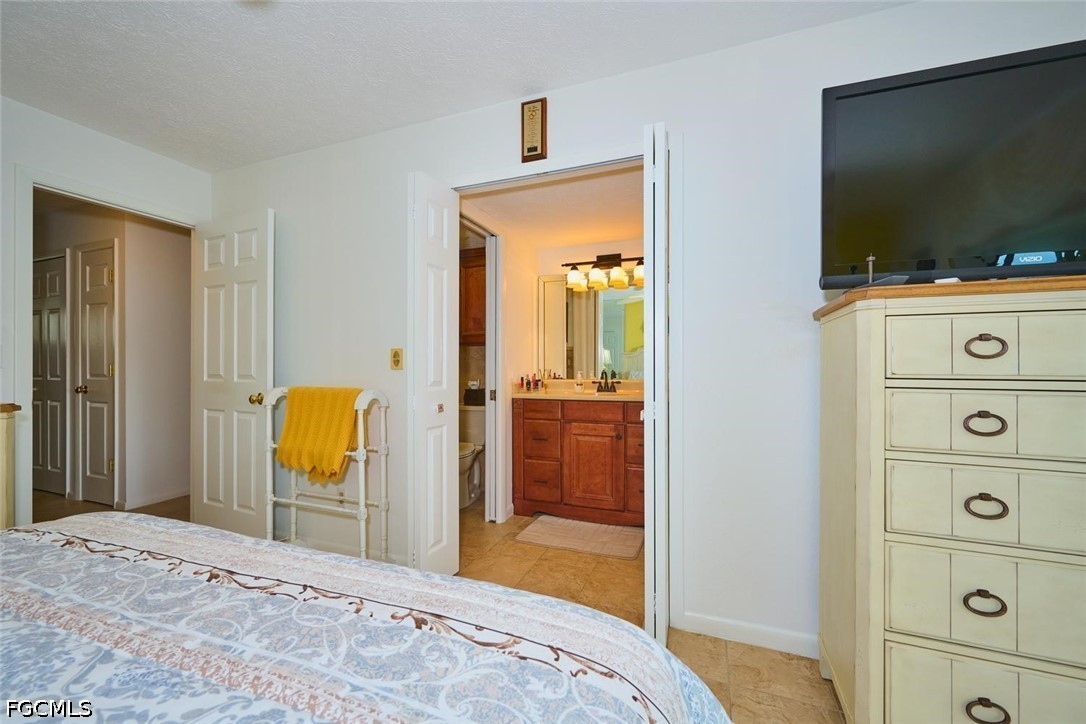 Bedroom with patterned bedding and open doors to an ensuite bathroom with a wood vanity.