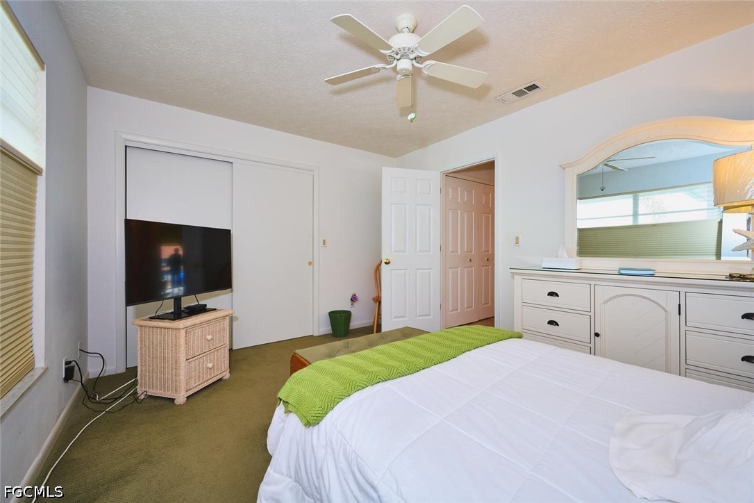 Furnished bedroom with a green bed throw, ceiling fan, and built-in dresser with a large mirror.