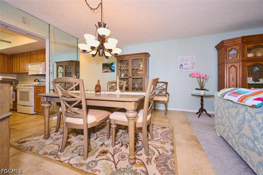 Dining room with a wooden table, patterned rug, chandelier, and kitchen visible to the left.
