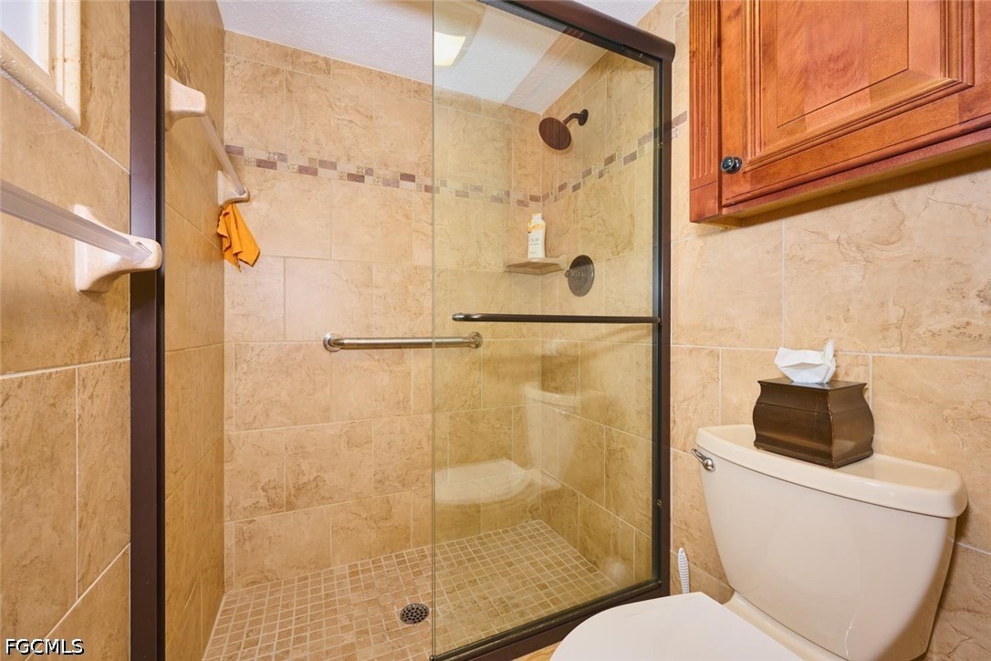Bathroom with a glass-enclosed tiled shower, mosaic floor, and wooden wall cabinet.