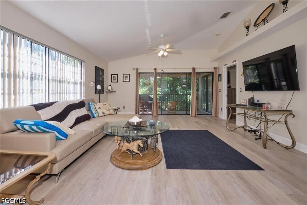 Furnished living room with a beige sectional, glass coffee table, and sliding doors to a leafy patio.
