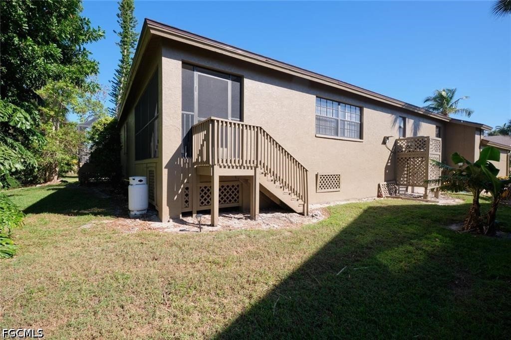 Tan house exterior with a raised wooden staircase and landing beside a grassy yard.