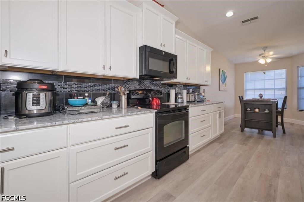 Kitchen with white cabinets, dark tile backsplash, stainless steel appliances, and a dining table by the windows.