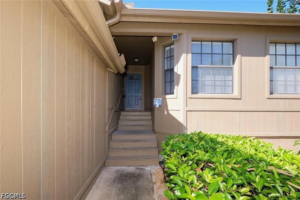 Home entrance with a blue front door, wooden steps, beige siding, and shrubs.