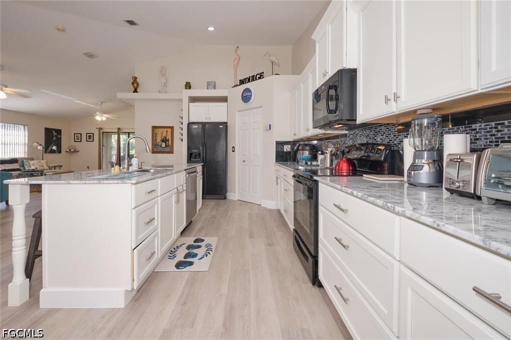 Kitchen with white cabinetry, gray countertops, a large island, and dark appliances opening to the living area.