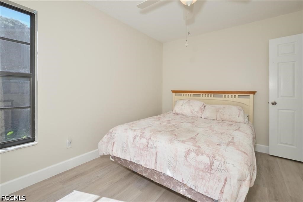 Bedroom with pale pink Paris-themed bedding, a black-framed window, and light wood-look flooring.