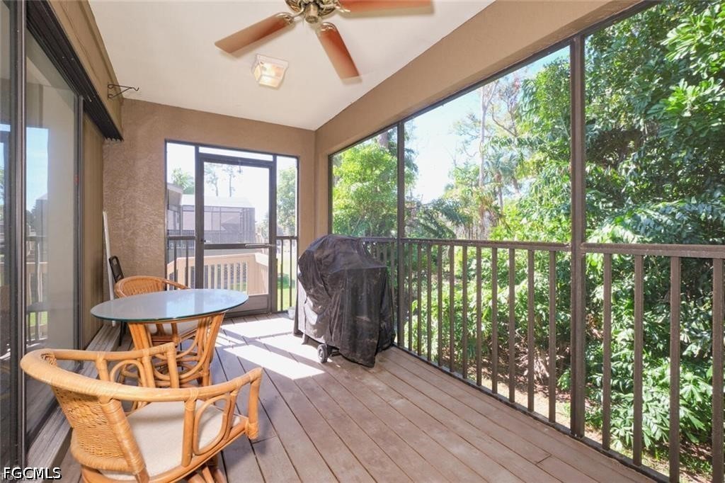 Screened lanai with wicker seating and a covered grill overlooking leafy trees.