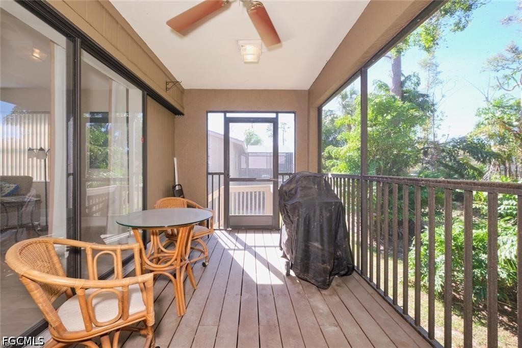 Screened-in patio with wicker dining furniture, a covered grill, and leafy greenery beyond the railing.