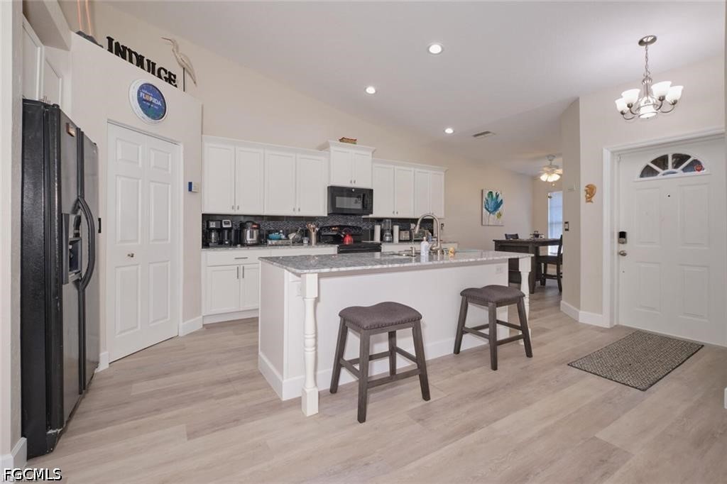 Kitchen with white cabinets, granite island, two stools, and dark appliances.