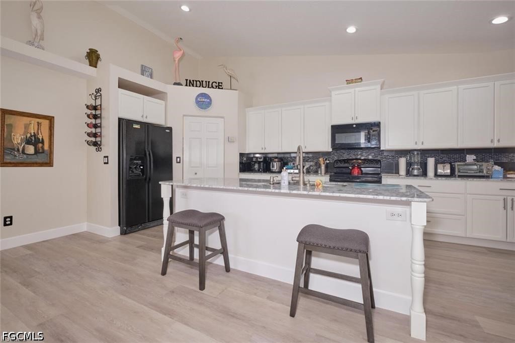 Kitchen with white cabinets, black appliances, and a large island with two upholstered stools.