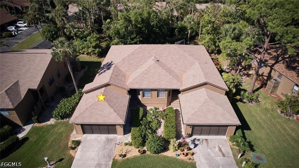 Aerial view of a tan home with two garages, a landscaped entrance, and mature trees.