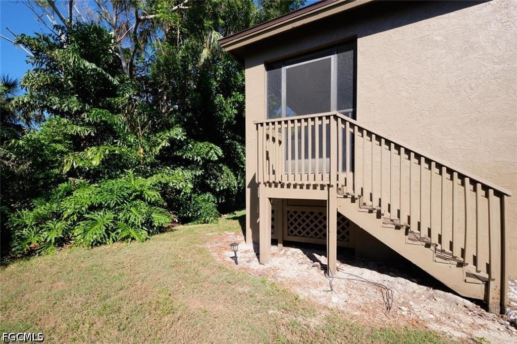 Beige stucco home with a raised wooden staircase and landing beside a large window.