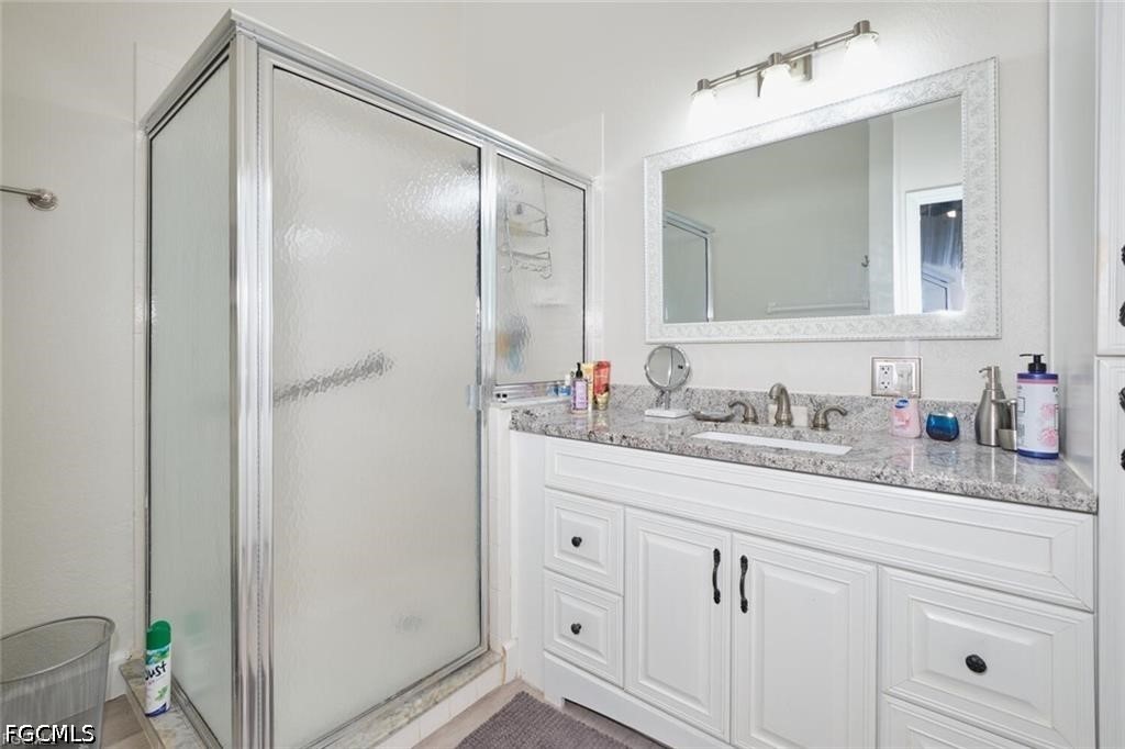 Bathroom with a white vanity, speckled stone counter, large mirror, and frosted-glass shower.