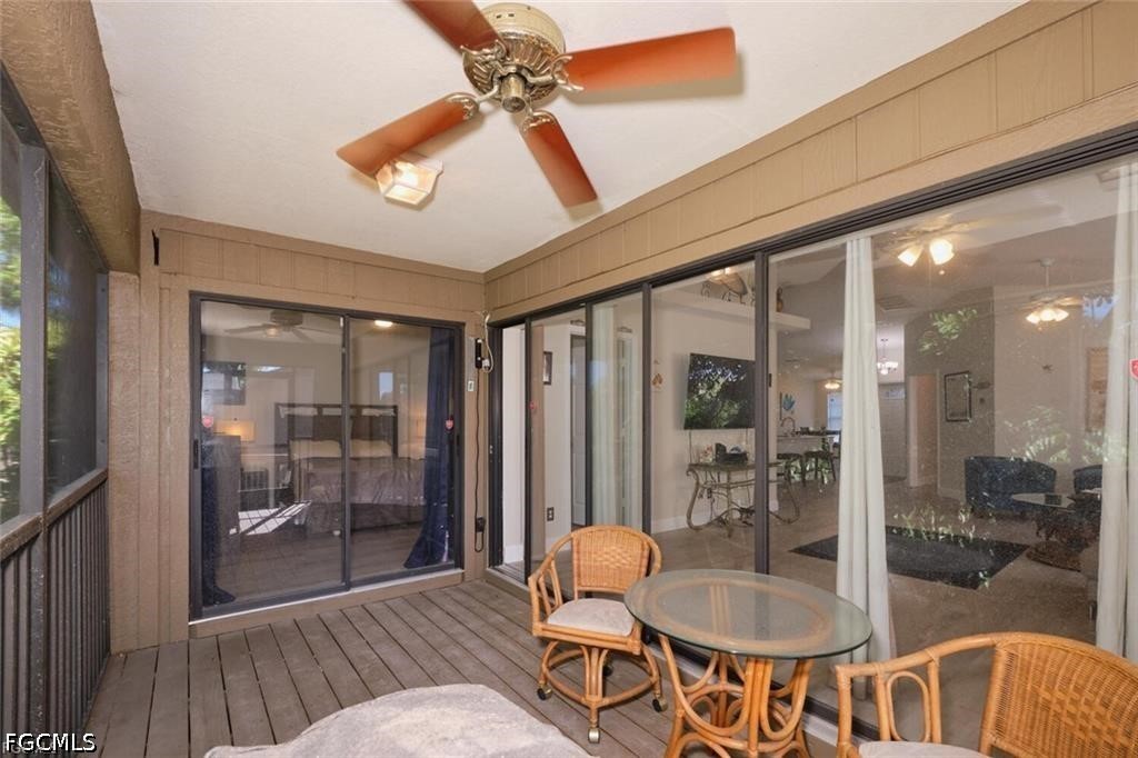 Covered patio with wicker seating, a glass-top table, ceiling fan, and sliding glass doors.