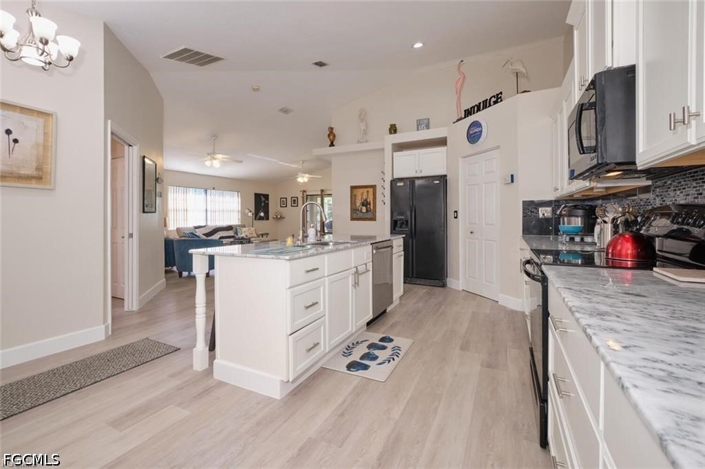Kitchen with a white island, stone countertops, dark appliances, and an open view to the living area.