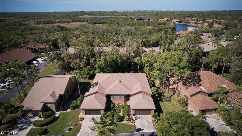 Aerial view of a tan-roofed home with attached garages amid a wooded neighborhood.