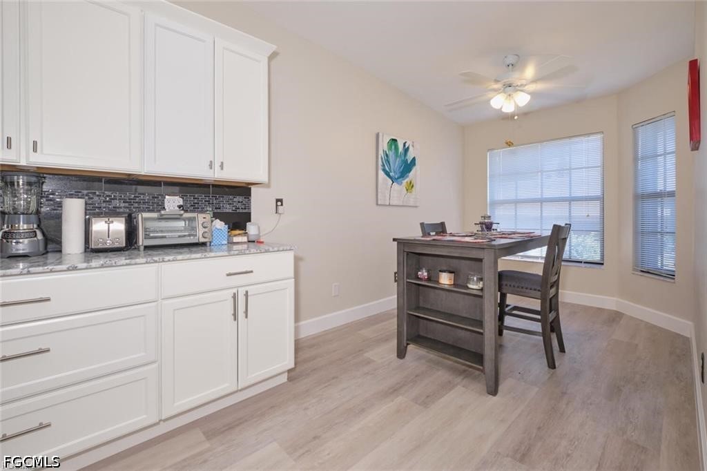 Kitchen and dining area with white cabinets, dark backsplash, and a table beside two windows.