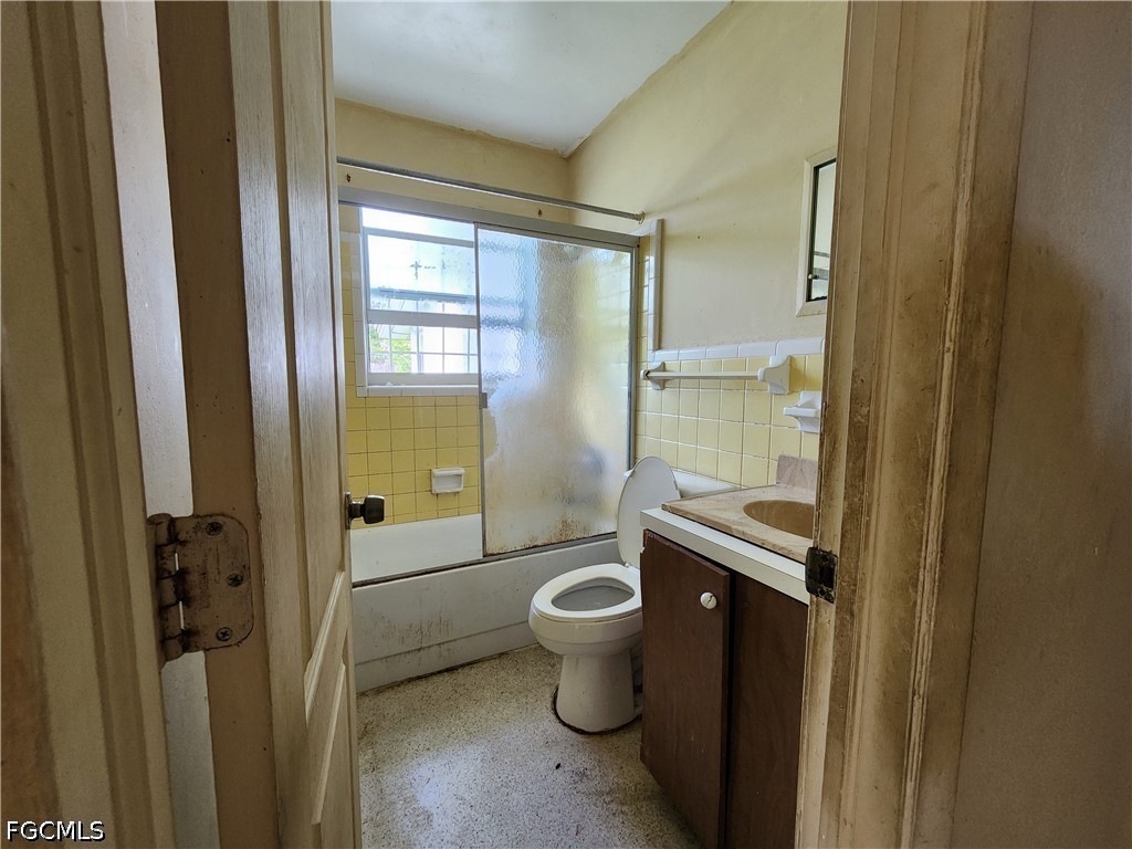 Bathroom with yellow tile, a frosted-glass tub enclosure, toilet, and dark wood vanity.