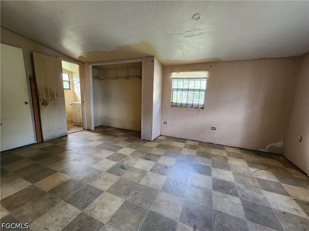 Vacant bedroom with an open closet, patterned tile floor, and damaged ceiling.