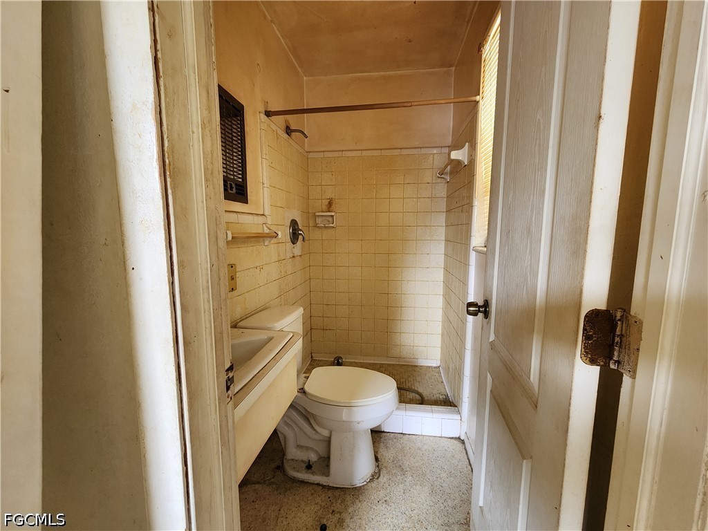 Bathroom with a toilet, small sink, and cream-tiled shower stall.