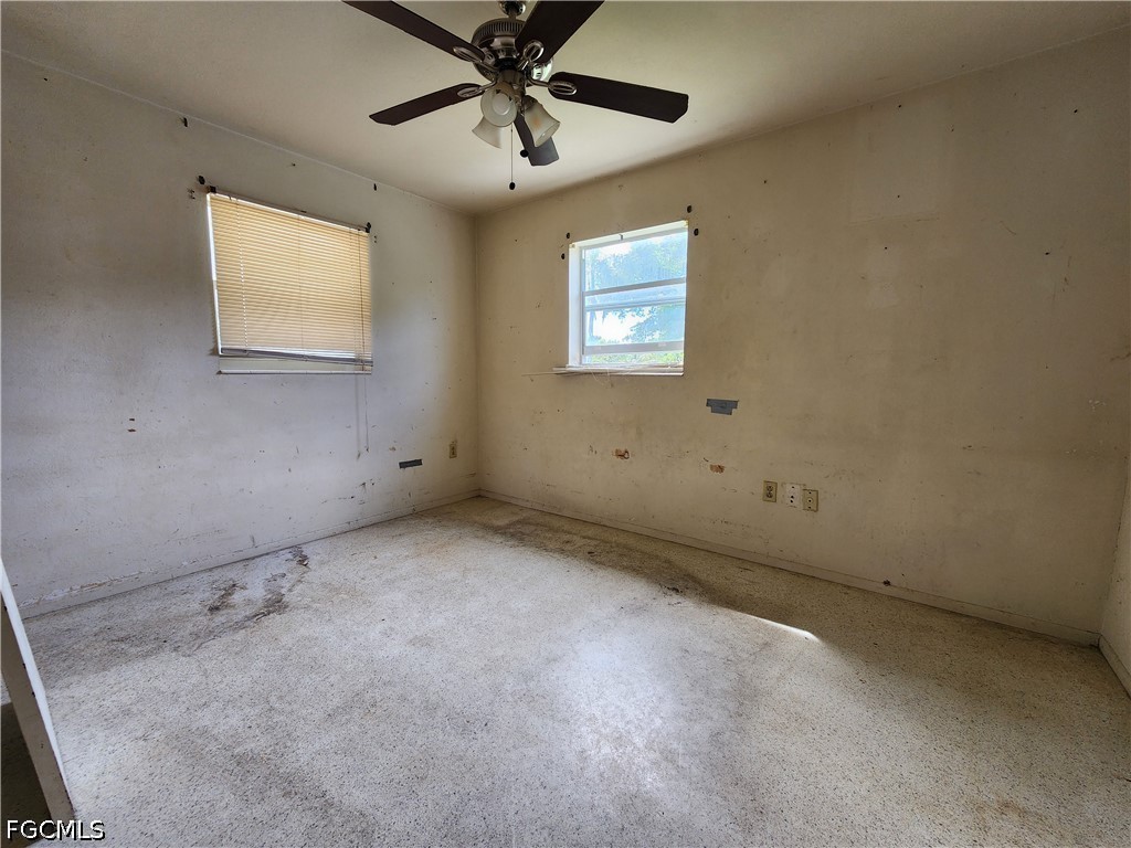 Empty room with stained carpet, scuffed walls, two windows, and a ceiling fan.