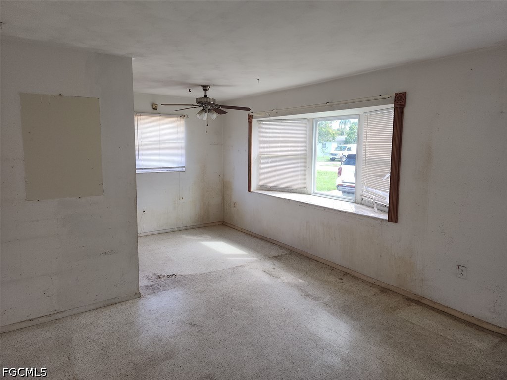 Empty room with a ceiling fan, worn walls, and windows with blinds.
