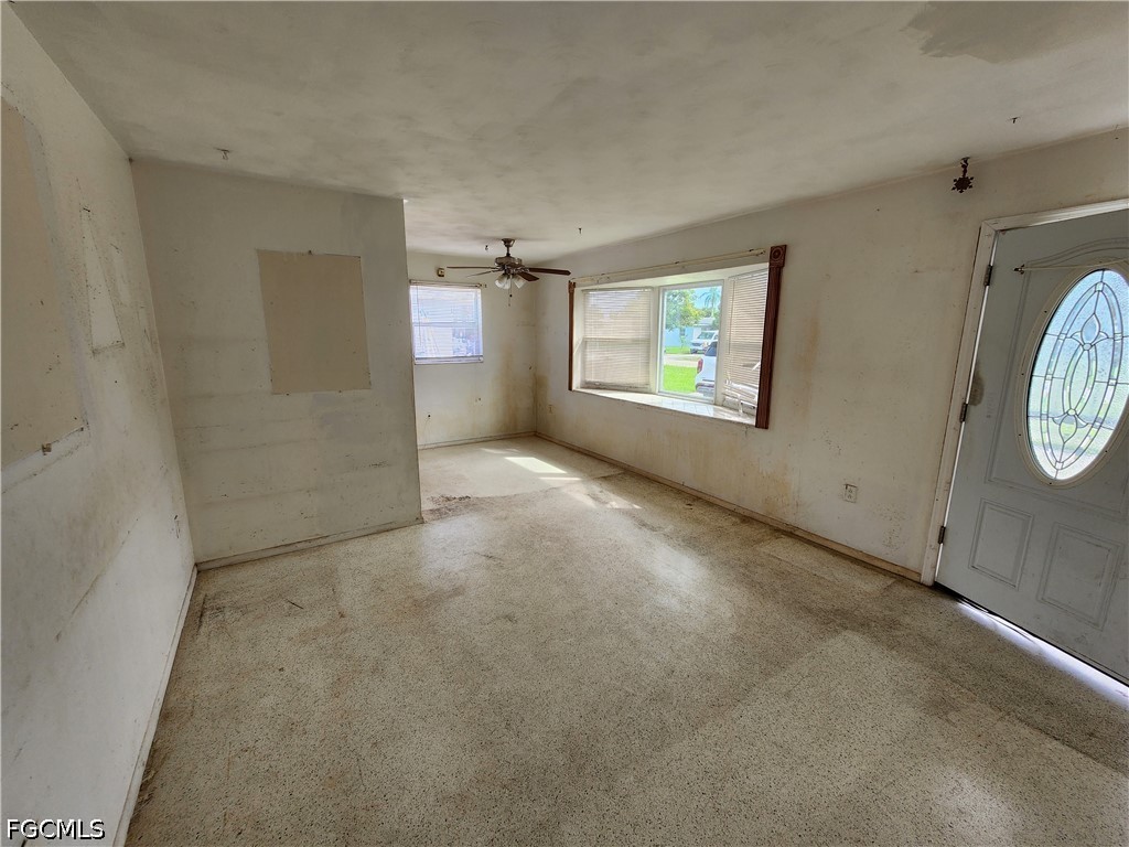 Vacant room with a ceiling fan, large windows, and a front door with oval glass.