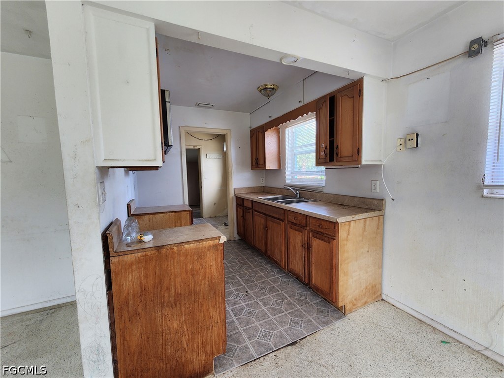 Vacant kitchen with worn wood cabinets, a double-basin sink, and patterned tile flooring.