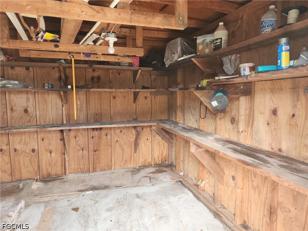 Wood-paneled storage shed interior with wall shelves, a long workbench, and exposed roof framing.